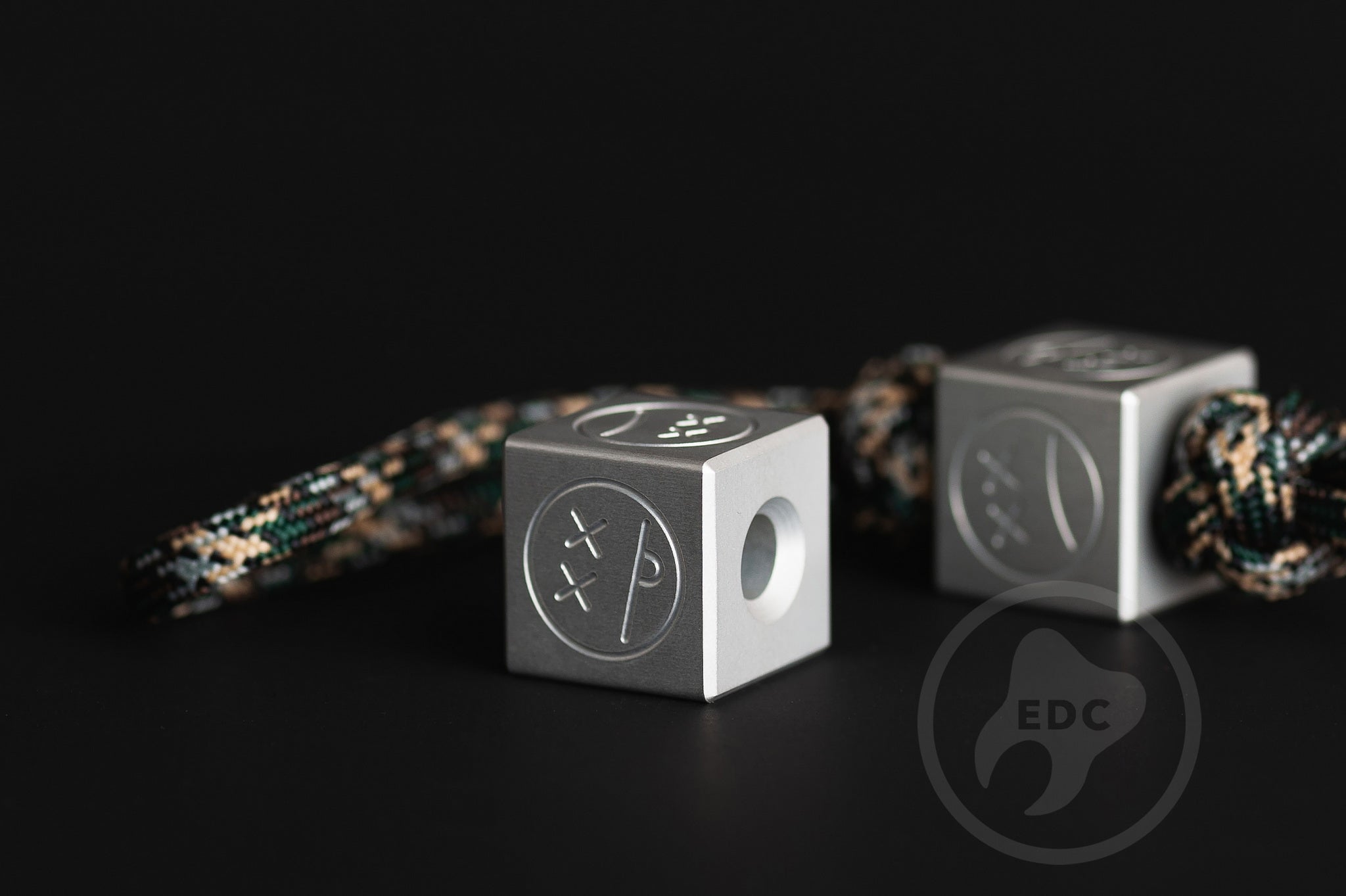 Grey aluminum Sad Face Cube paracord accessory.