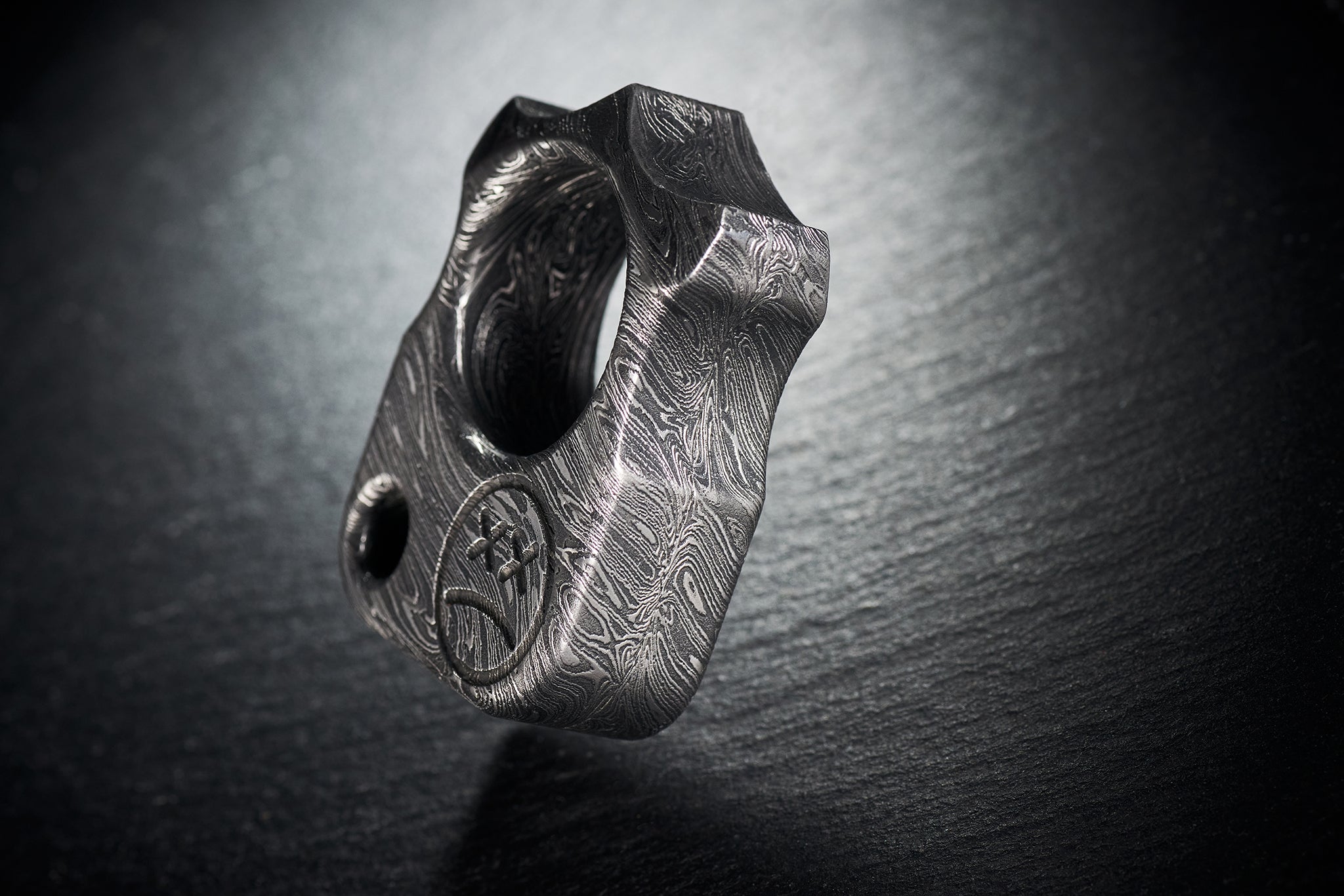 Close up of hand-etched Sad Face logo on high-contrast Damascus steel-3