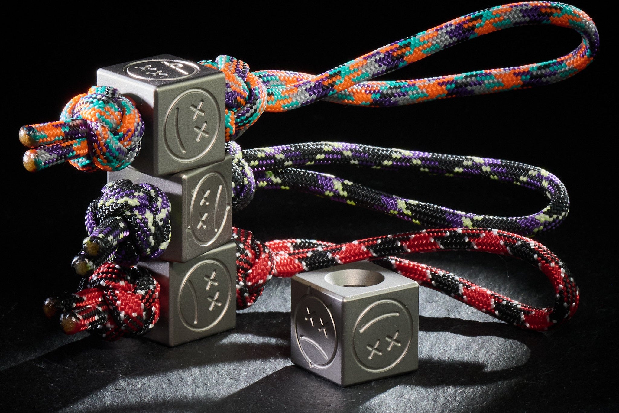 Custom folding knife featuring the Titanium Sad Face Cube on a paracord lanyard.-1