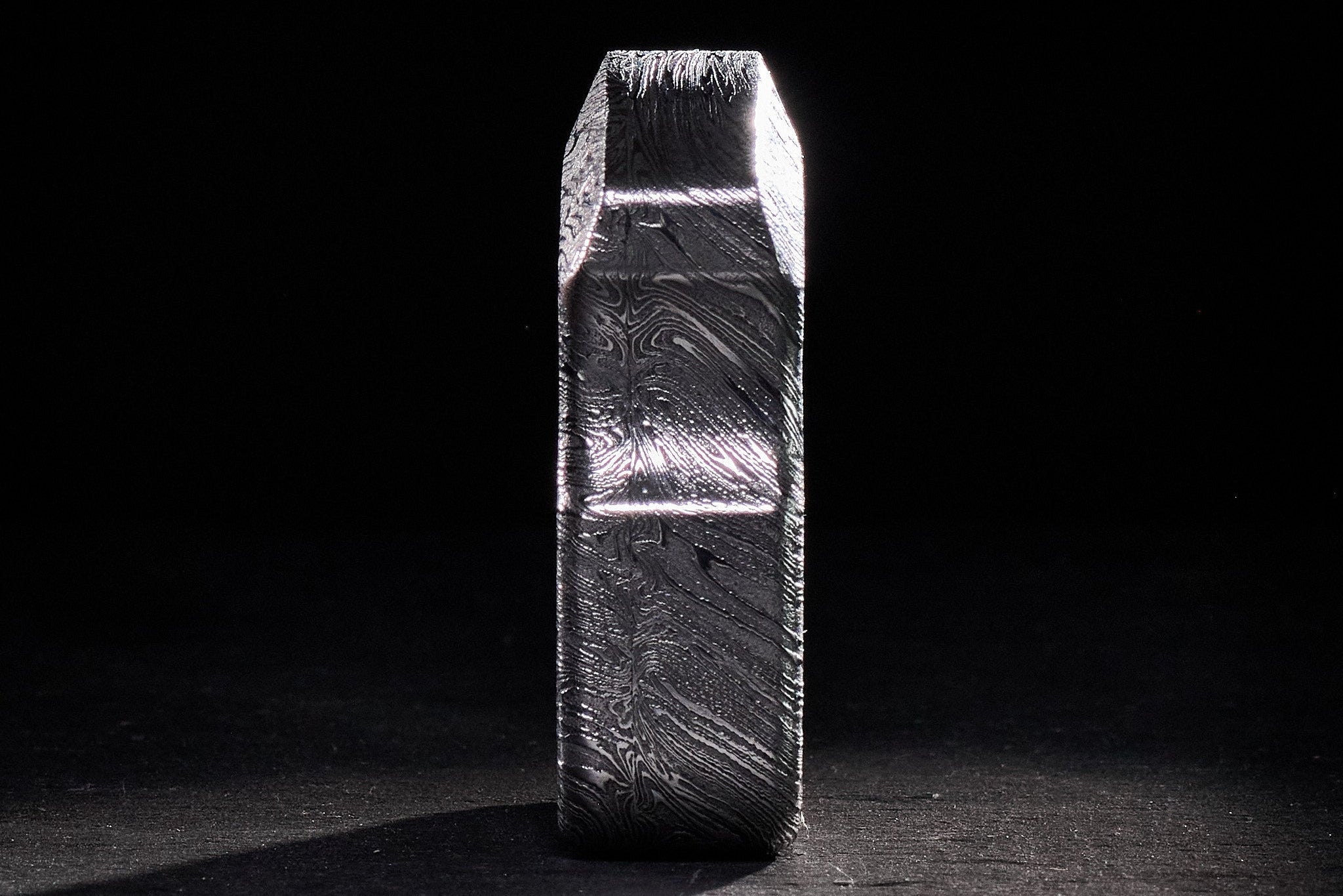 Close-up of high-contrast acid-etched layers on a custom Damascus steel tool.